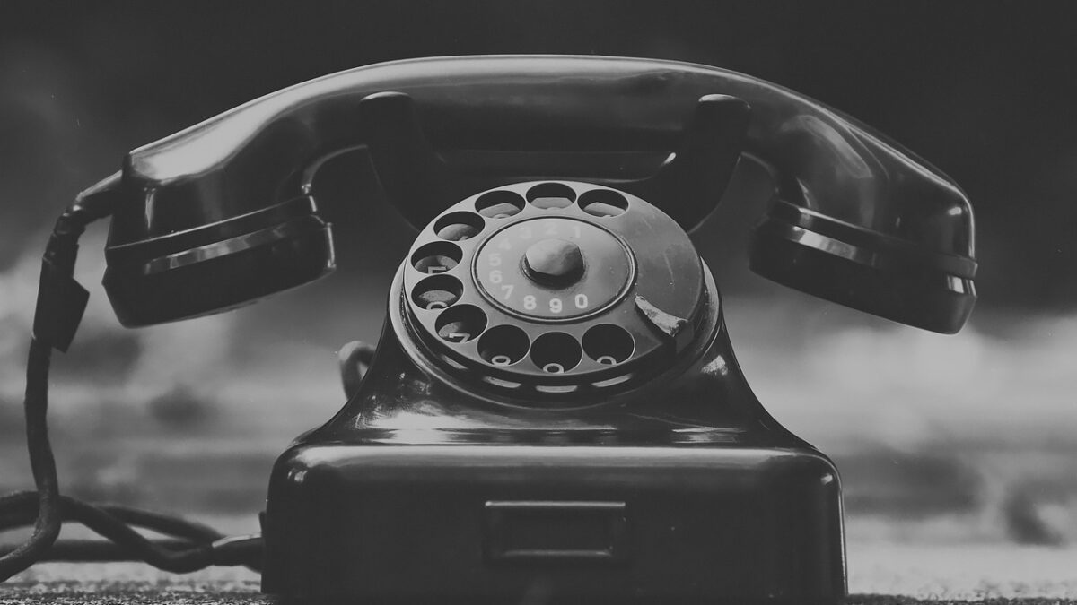 Téléphone fixe vintage à cadran rotatif, en noir et blanc, posé sur une surface sombre au premier plan.