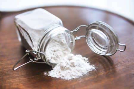 Glass jar tipped over with white flour spilling onto a wooden surface, ideal for baking themes.