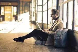 Voyages professionnels : le guide stratégique pour optimiser votre temps et votre argent Man sitting by a window at a Budapest train station, working on his laptop with sunlight streaming through.