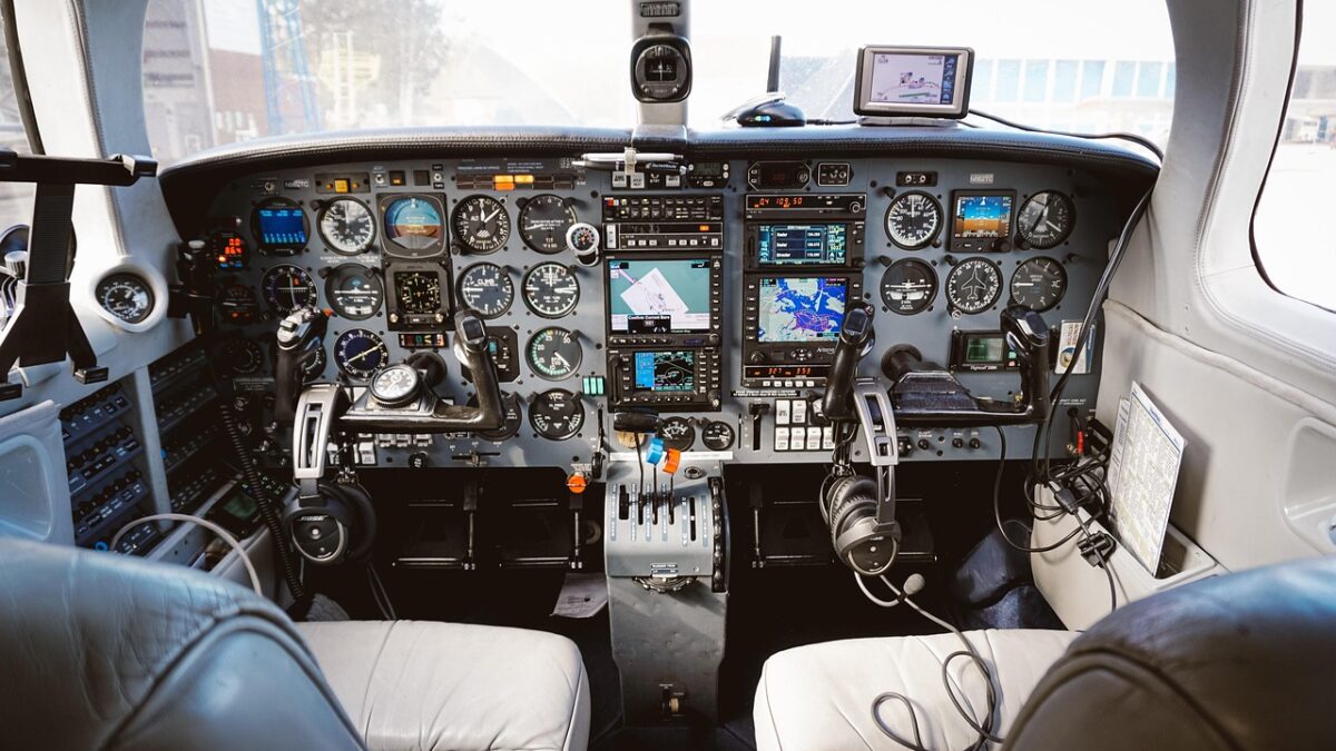 Cockpit d'un petit avion monomoteur : tableau de bord avec instruments analogiques, deux écrans GPS et casques audio sur les sièges en cuir.