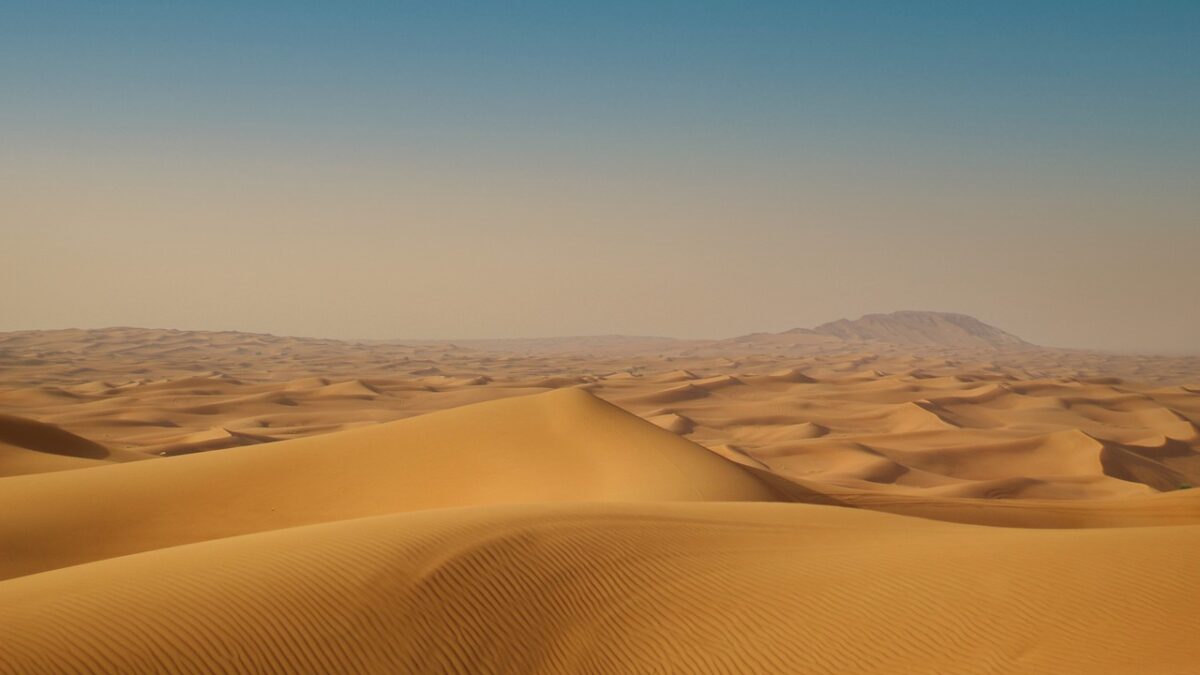 Dunes de sable ondulées sous un ciel bleu qui s'éclaircit vers l'horizon, sans aucune construction visible.