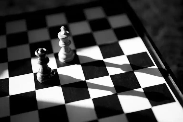 Les meilleurs jeux qui mettent au défi et stimulent votre cerveau pour une meilleure santé Black and white chess pieces casting long shadows on a chess board, creating a dramatic and strategic mood.