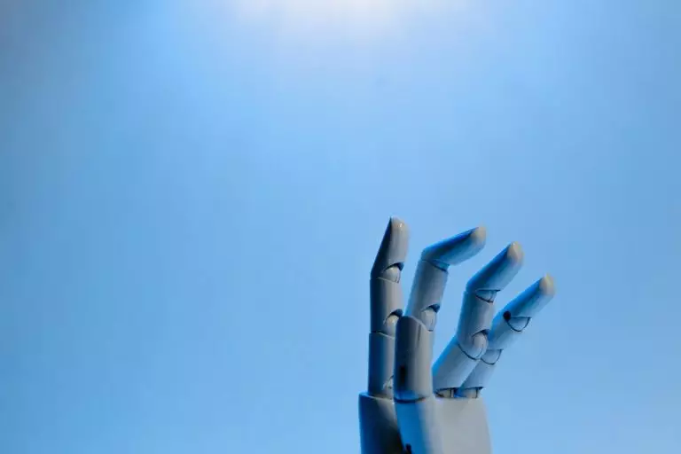 Analyse des données alimentée par l’IA : Le secret de la croissance des entreprises Robotic hand with articulated fingers reaching towards the sky on a blue background.
