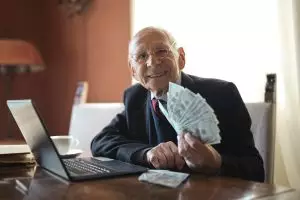 Préparer sa retraite en Suisse : conseils pratiques pour une transition après une carrière réussie Happy senior businessman showing cash at his desk with a laptop, indoors.