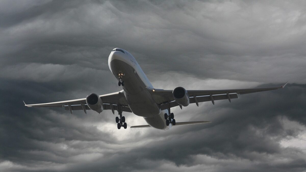 Un avion de ligne bimoteur gros-porteur, probablement un Airbus A330, en montée contre un ciel nuageux sombre, train d'atterrissage sorti.