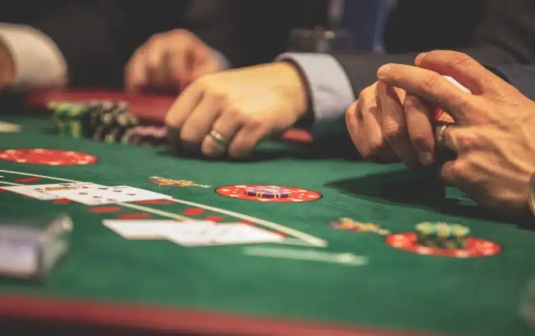 La montée des jeux de casino à compétences : vers la fin du pur hasard ? Hands playing blackjack in a casino setting with cards and chips on a green table.