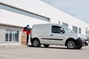 Dernier kilomètre : comment les grandes surfaces automatisent la livraison alimentaire en zone urbaine A delivery driver wearing a face mask unloads packages from a van outside a modern building.