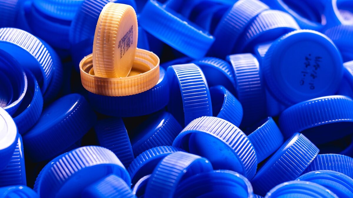 Amas de bouchons de bouteilles en plastique bleus, avec un bouchon jaune orangé dressé au centre.