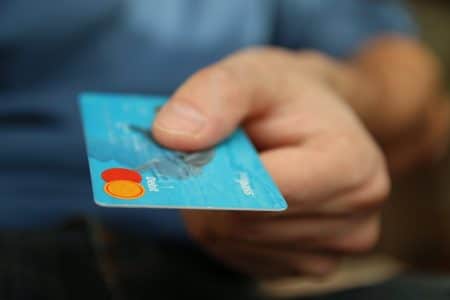 E-commerce 2025 : les tendances qui définiront l’expérience d’achat A close-up shot of a hand offering a blue debit card for payment.