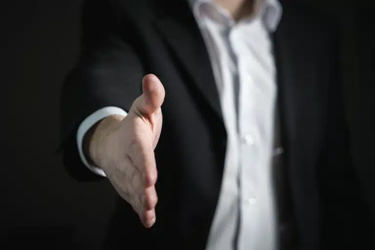 Marketing de réseau 2.0 : l’ère digitale révolutionne le MLM Close-up of a businessman extending hand for a handshake, symbolizing agreement and partnership.