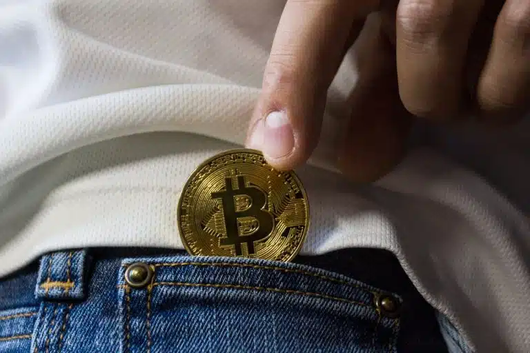 IA, blockchain, cloud… : les tendances tech à suivre de près Close-up of hand putting Bitcoin in jeans pocket symbolizing cryptocurrency savings.