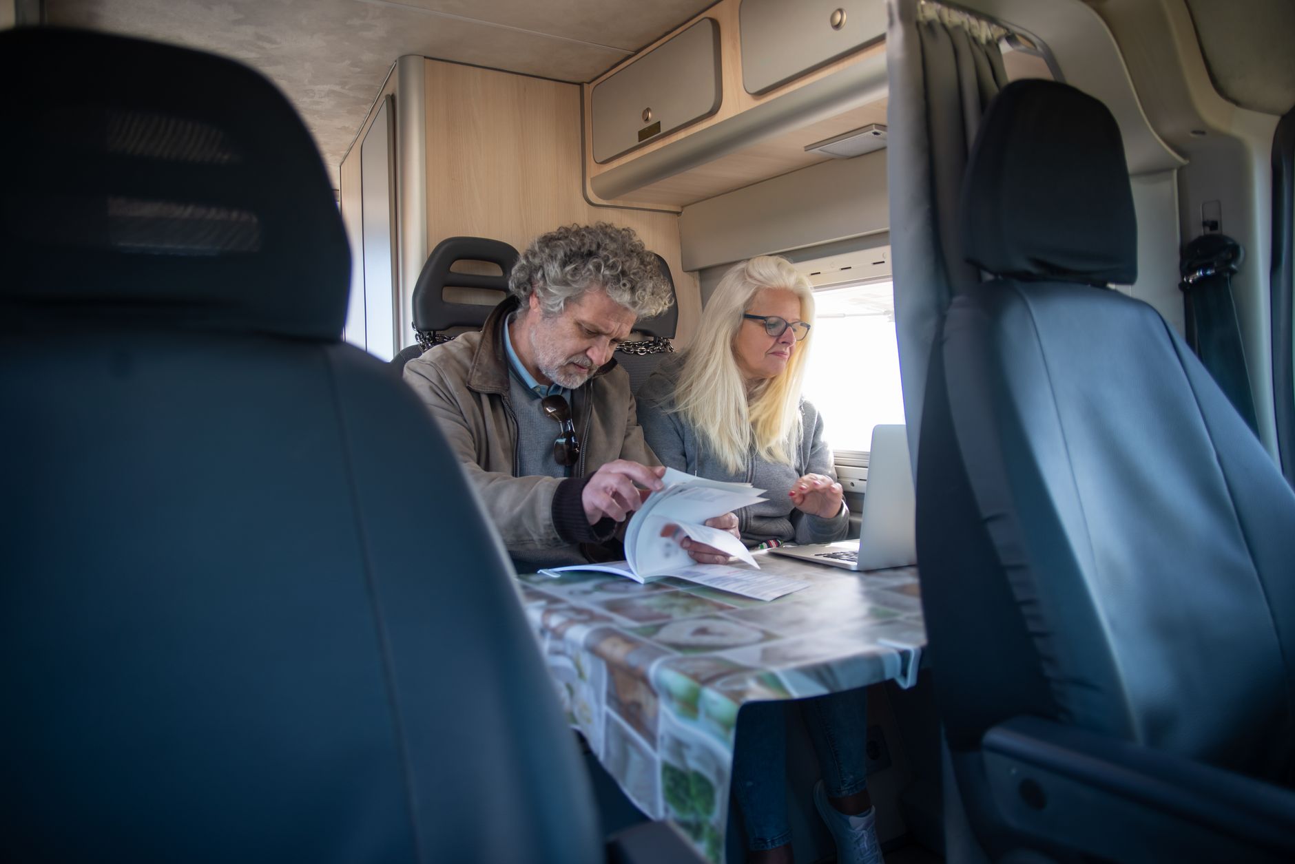 Un homme et une femme aux cheveux gris et blonds consultent des documents et un ordinateur portable à une table dans un fourgon aménagé.